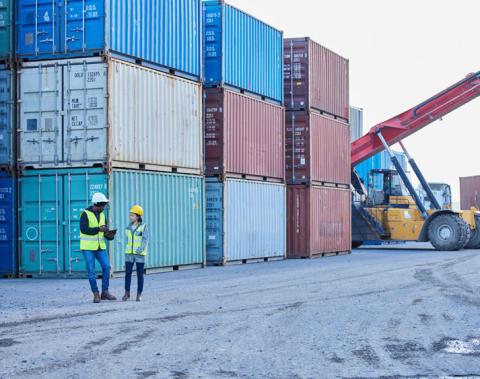 two workers in shipping yard surrounded by containers