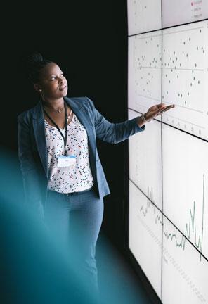 Businesswoman giving a presentation at a business conference. Looking at a large video screen with charts and graphs